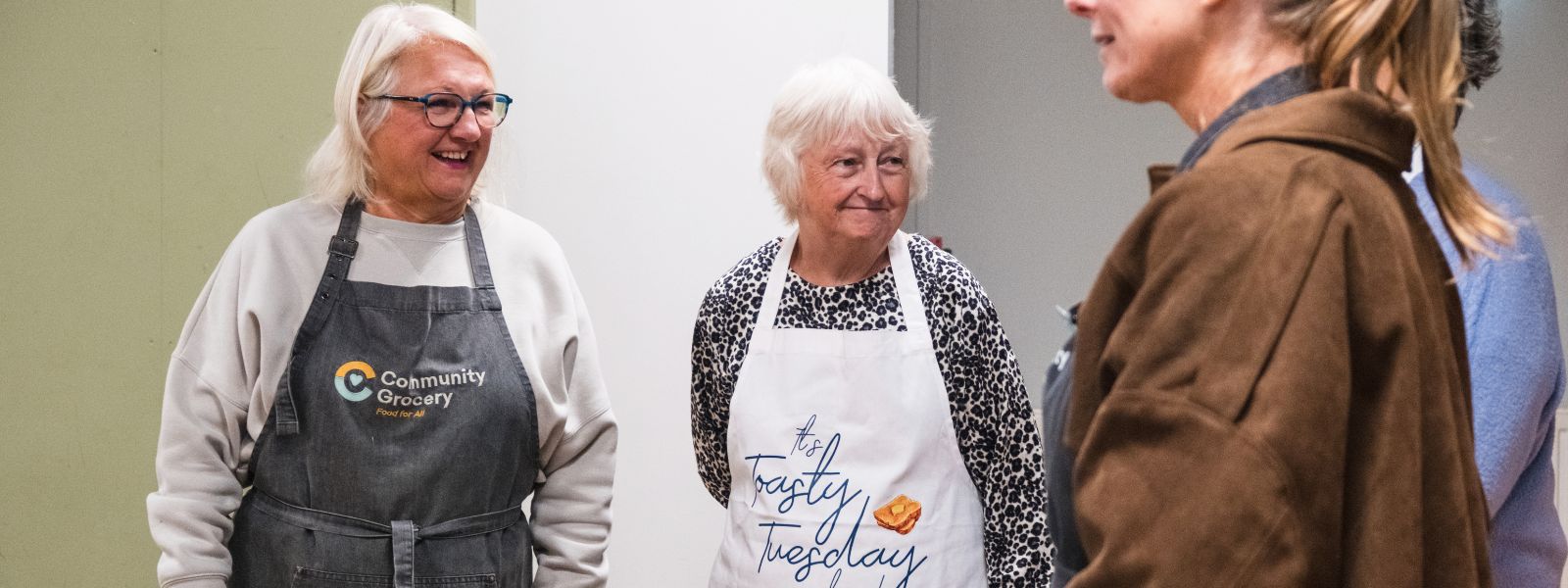 Volunteers in aprons from the Grocery and church chat with members of the community.